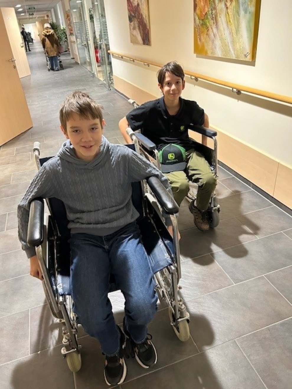 Zwei Buben fahren mit Rollstühlen am Gang