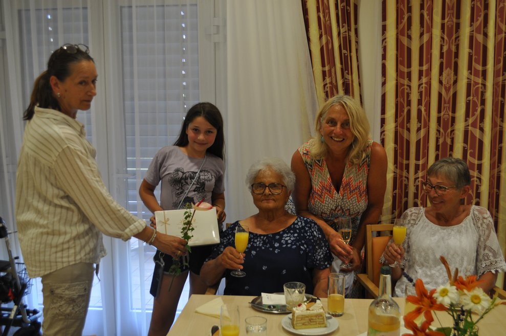 einige Menschen bei einer Geburtstagsfeier mit Blumen, Sekt und Pralinen