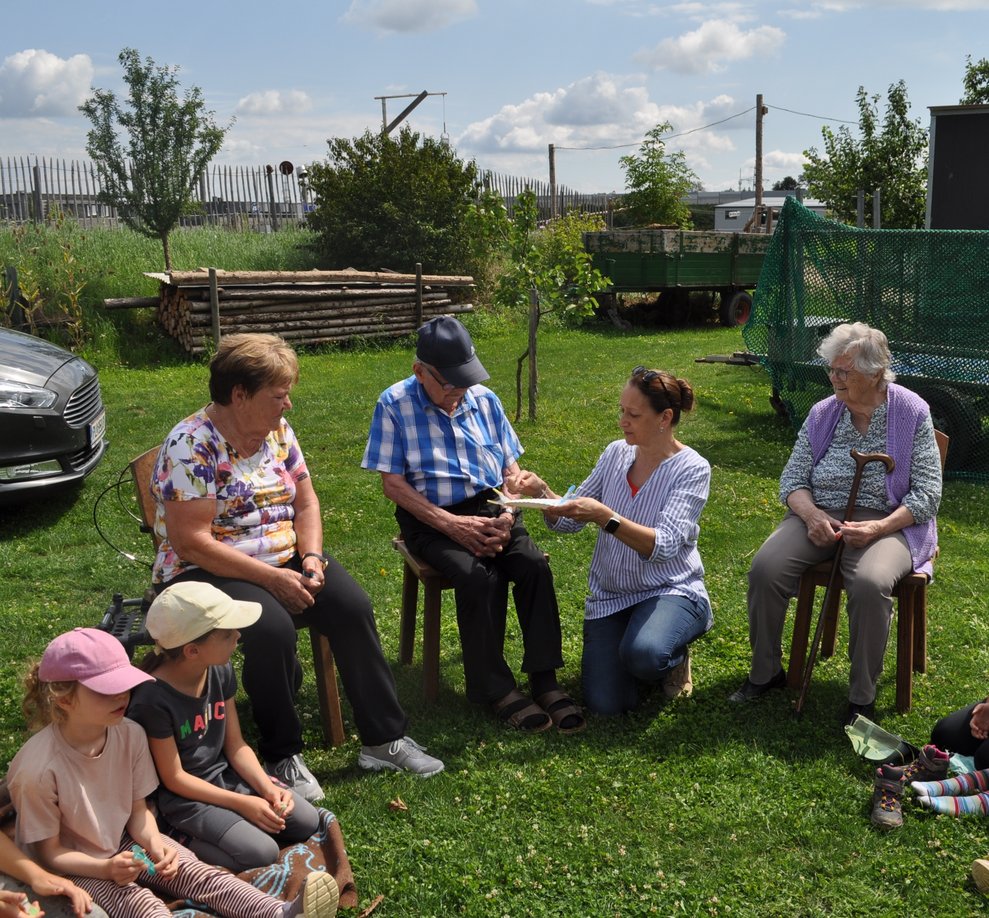 eine Gruppe von älteren Menschen und Kindern sitzt in der Wiese im Kreis