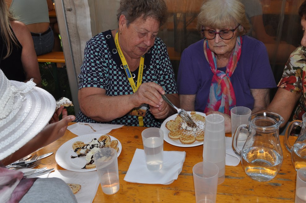 eine Frau hilft einer älteren Dame beim Waffeln zerteilen