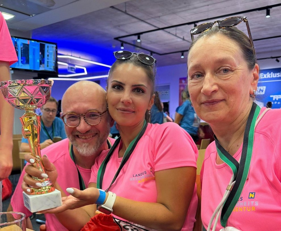ein Mann und zwei Frauen mit pinken Sport T-Shirts, Medaillen und Pokal