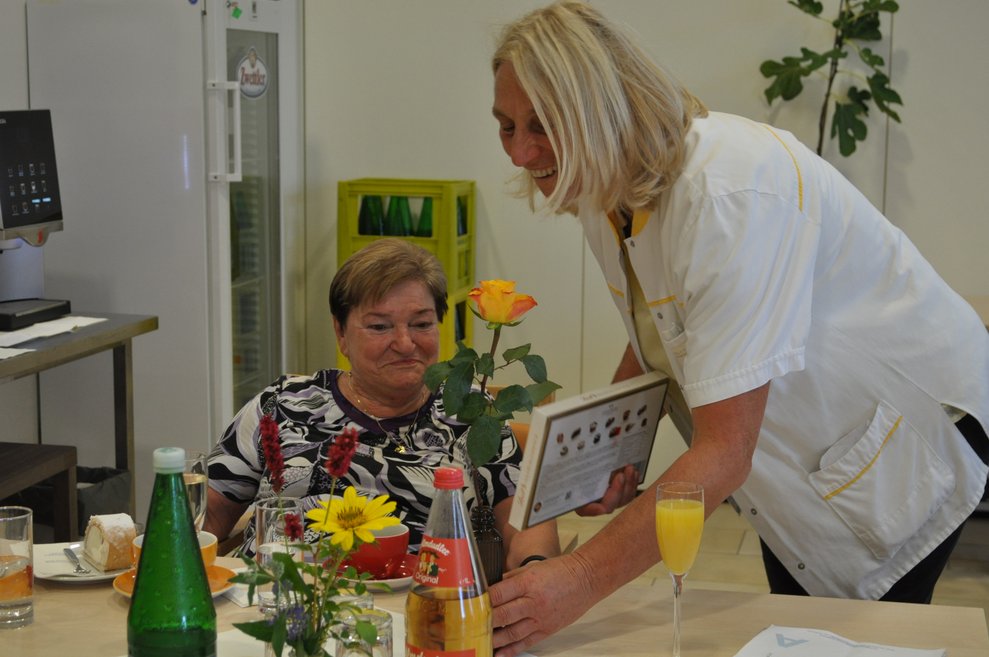 eine Dame überreicht einer älteren Frau Pralinen zum Geburtstag
