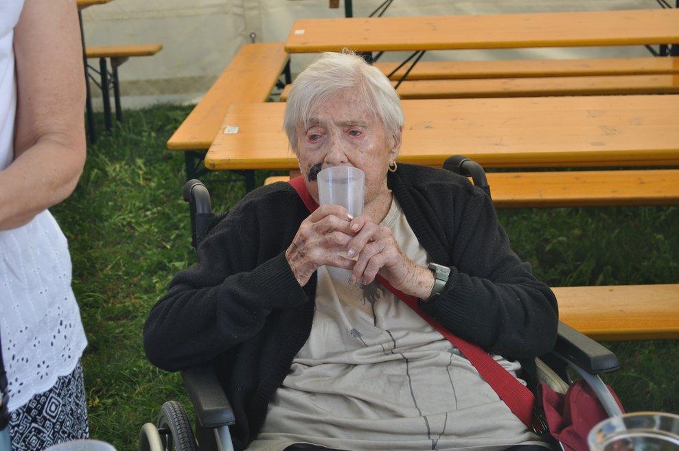 eine ältere Frau trinkt aus einem Plastikbecher