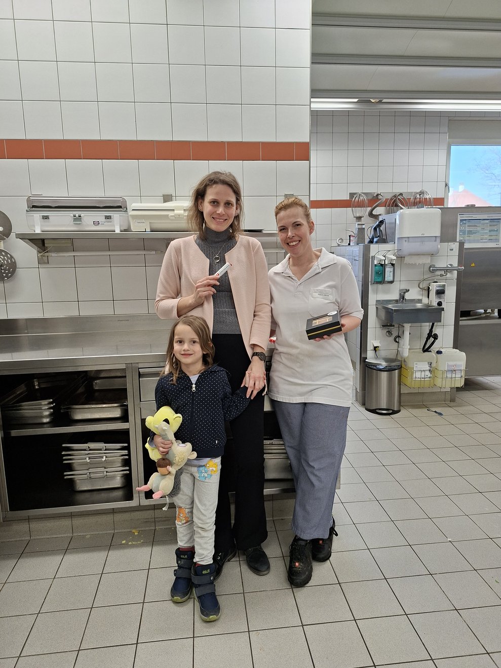 2 Mitarbeiterinnen und 1 Mädchen in der Küche bei der Übergabe der Duplo Riegel.