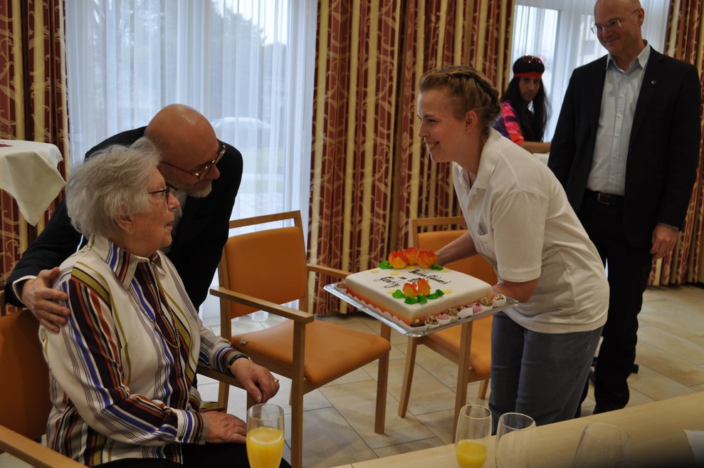 eine Frau überreicht eine Torte zum 101. Geburtstag
