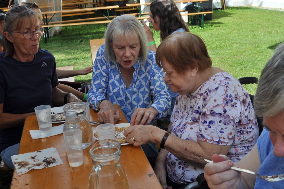 eine Frau hilft einer älteren Dame beim Waffeln essen