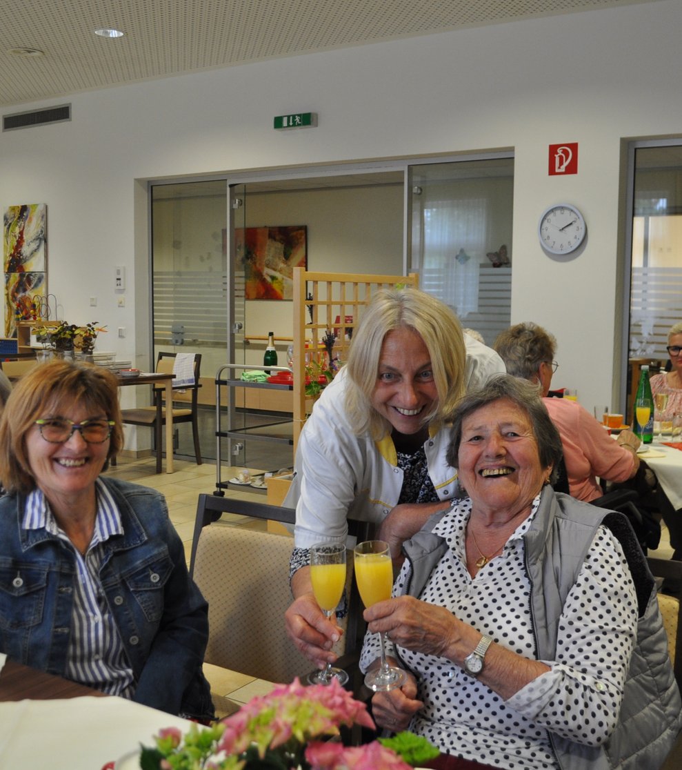 einige Menschen bei einer Geburtstagsfeier mit Blumen, Sekt und Pralinen