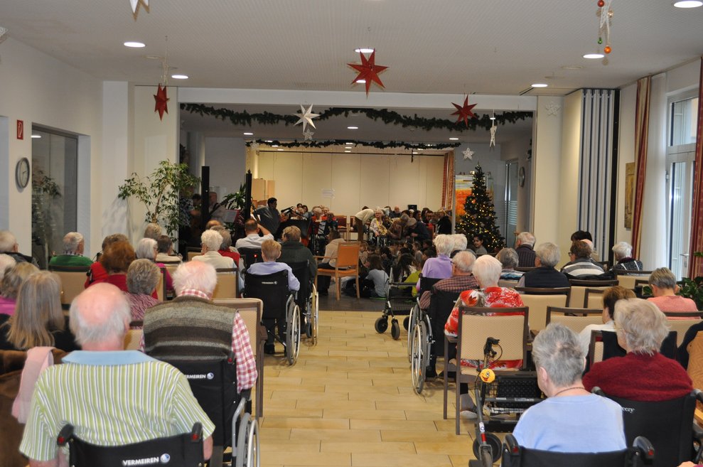 Blick auf die Bühne, man sieht viele ältere Menschen im Rollstuhl oder Rollator sitzen und alles ist weihnachtlich dekoriert