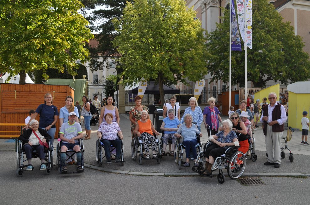 einige ältere Menschen mit Rollstühlen und Rollatoren vor dem Gelände der NÖKISS