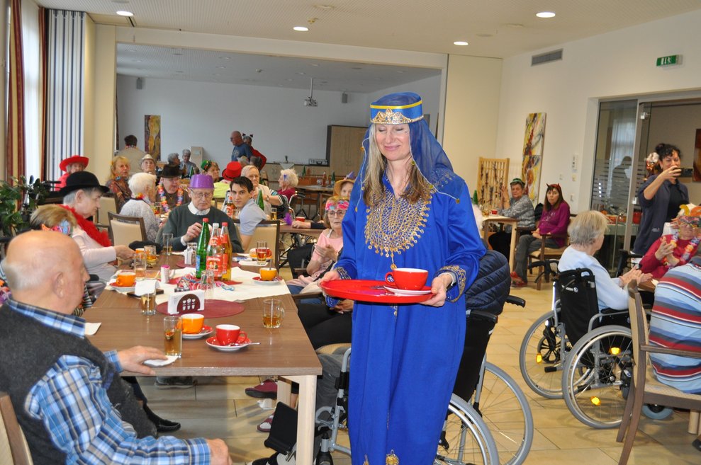 eine Frau als Orientalierin verkleidet serviert Bewohnerinnen und Bewohnern Kaffee