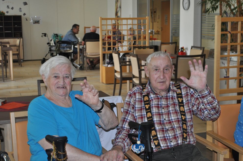 eine ältere Dame und ein älterer Herr im Kaffeehaus und winken her