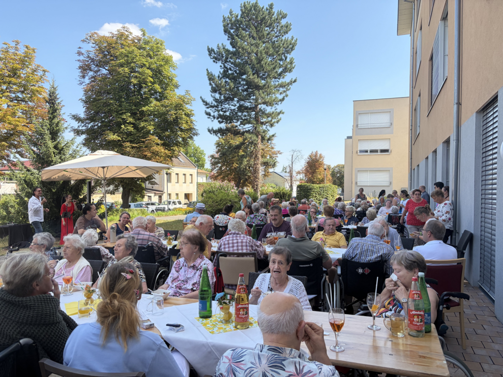 mehrere Personen sitzen auf Heurigengarnituren beim italienischen Nachmittag