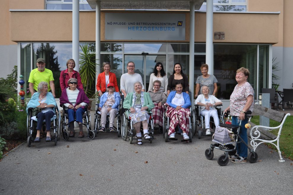 Mehrere Personen in Rollstühlen und Rollatoren vor dem Pflegeheim