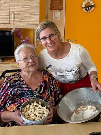 eine ältere Dame und eine jüngere mit zwei Keksdosen 