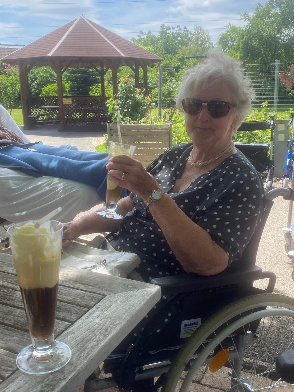 eine ältere Dame im Rollstuhl trinkt einen Eiskaffee
