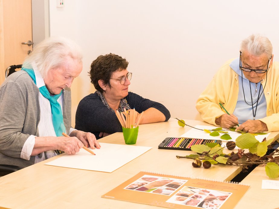 Eine Betreuerin mit 2 BewohnerInnen, die etwas malen.