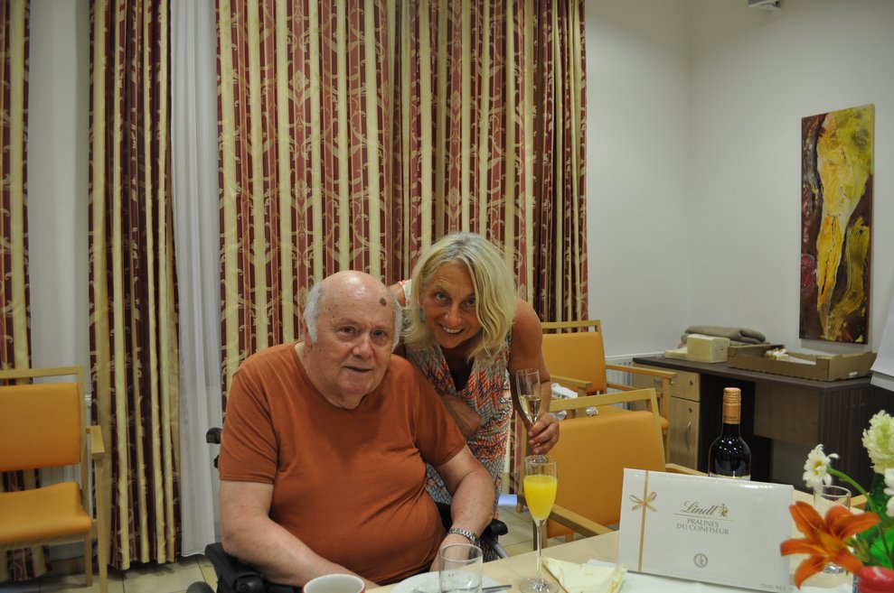 einige Menschen bei einer Geburtstagsfeier mit Blumen, Sekt und Pralinen