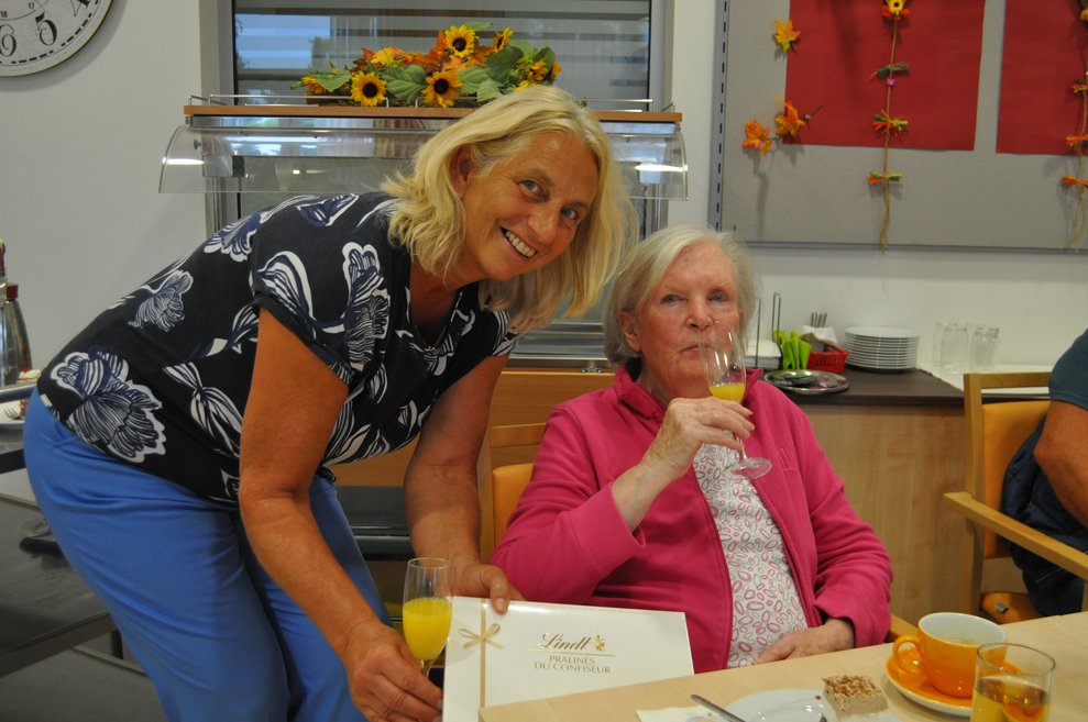 eine Dame und eine Bewohnerin stoßen zum Geburtstag mit Sekt Orange an