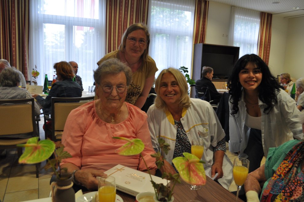 einige Menschen bei einer Geburtstagsfeier mit Blumen, Sekt und Pralinen