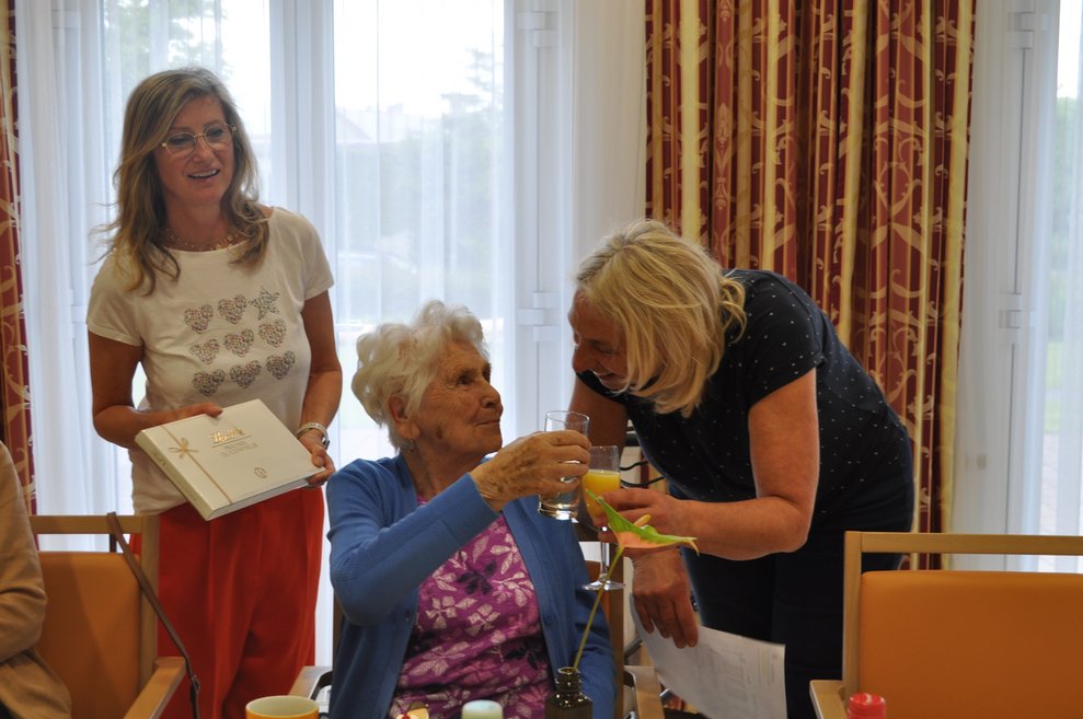 einige Menschen bei einer Geburtstagsfeier mit Blumen, Sekt und Pralinen