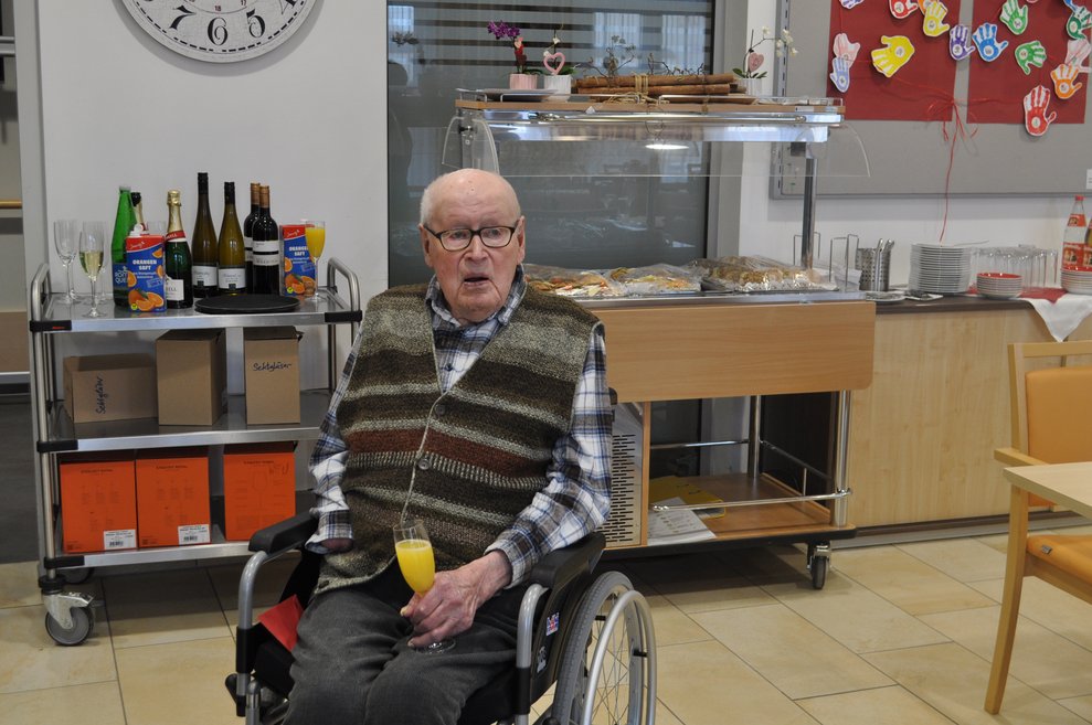 ein älterer Herr im Rollstuhl mit Sekt Orange Glas