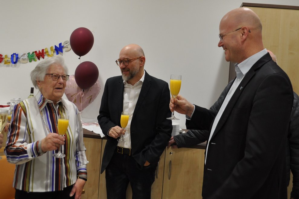 Zwei Herren und eine ältere Dame stoßen mit Sektgläsern an