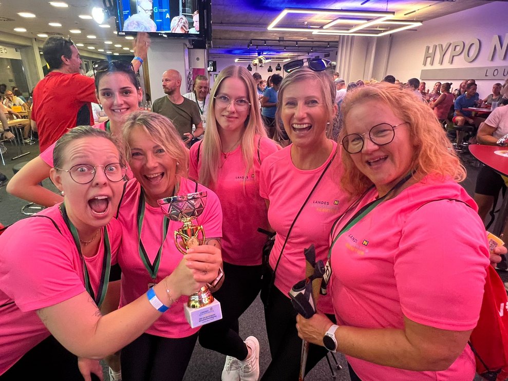 Mehrere Personen in pinken Sport T-Shirts jubelnd mit einem Pokal