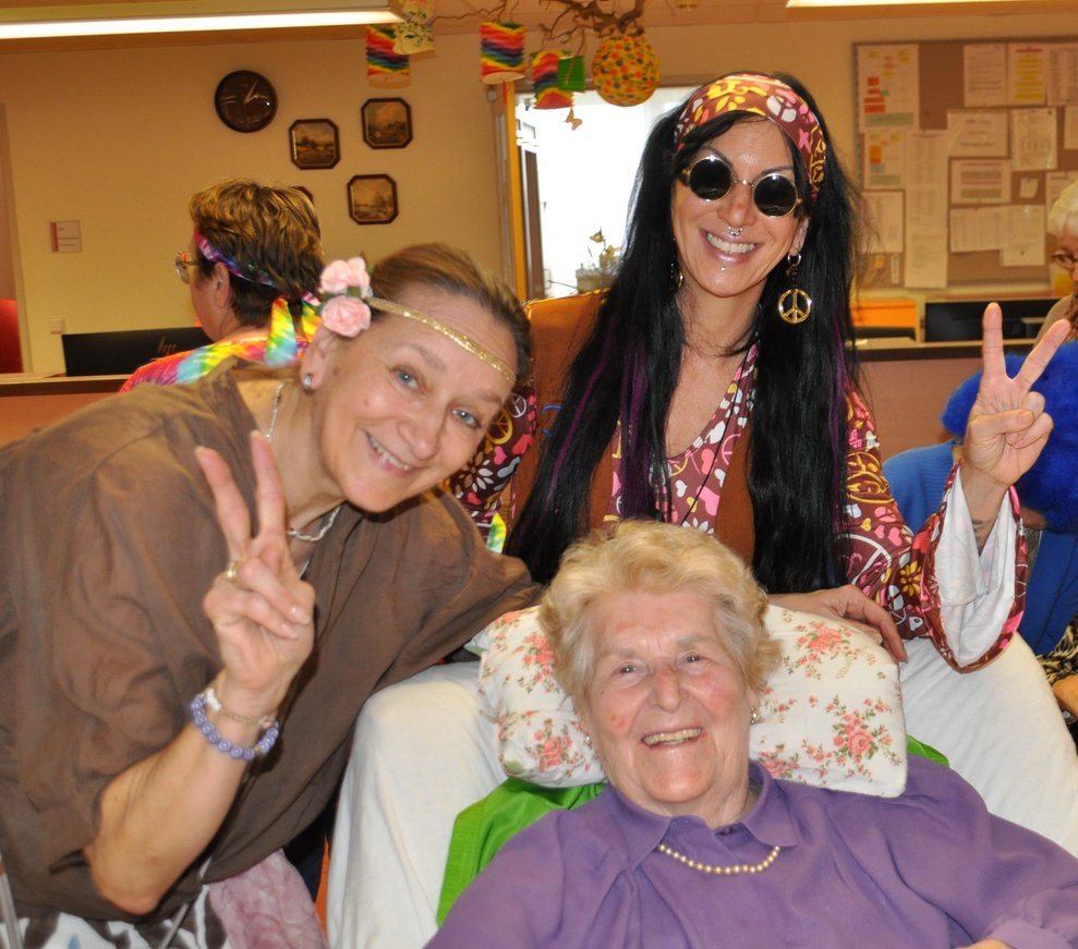 zwei Frauen sind als Hippies verkleidet und machen ein Foto mit einer Bewohnerin 