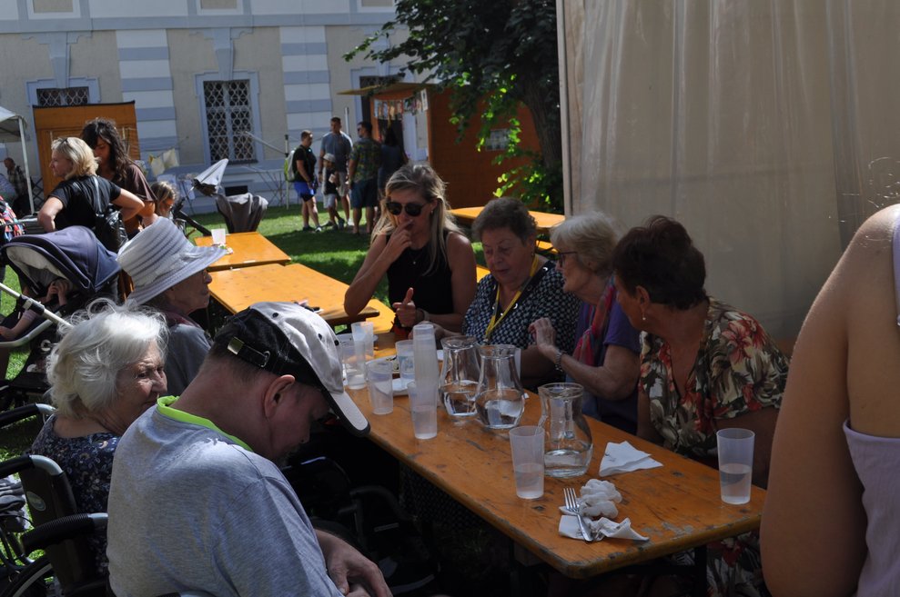 einige ältere Menschen sitzen auf Heurigen Garnituren und trinken und essen