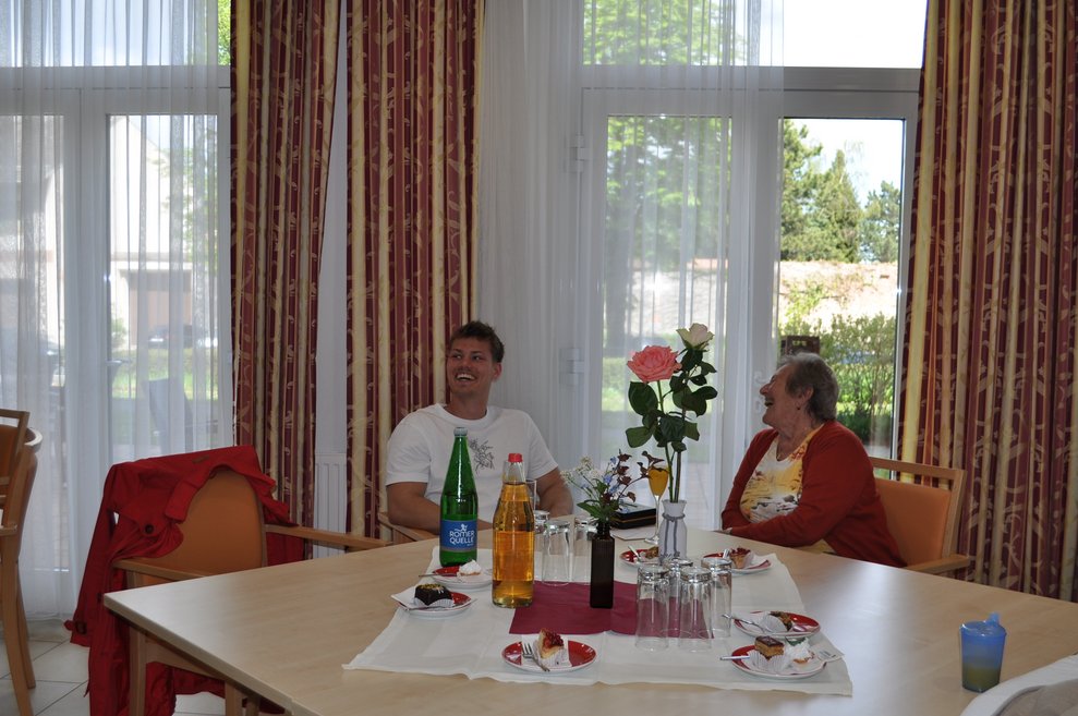 eine ältere Dame und ein jüngerer Mann sitzen bei Tisch, der Tisch ist schön gedeckt für die Geburtstagsfeier