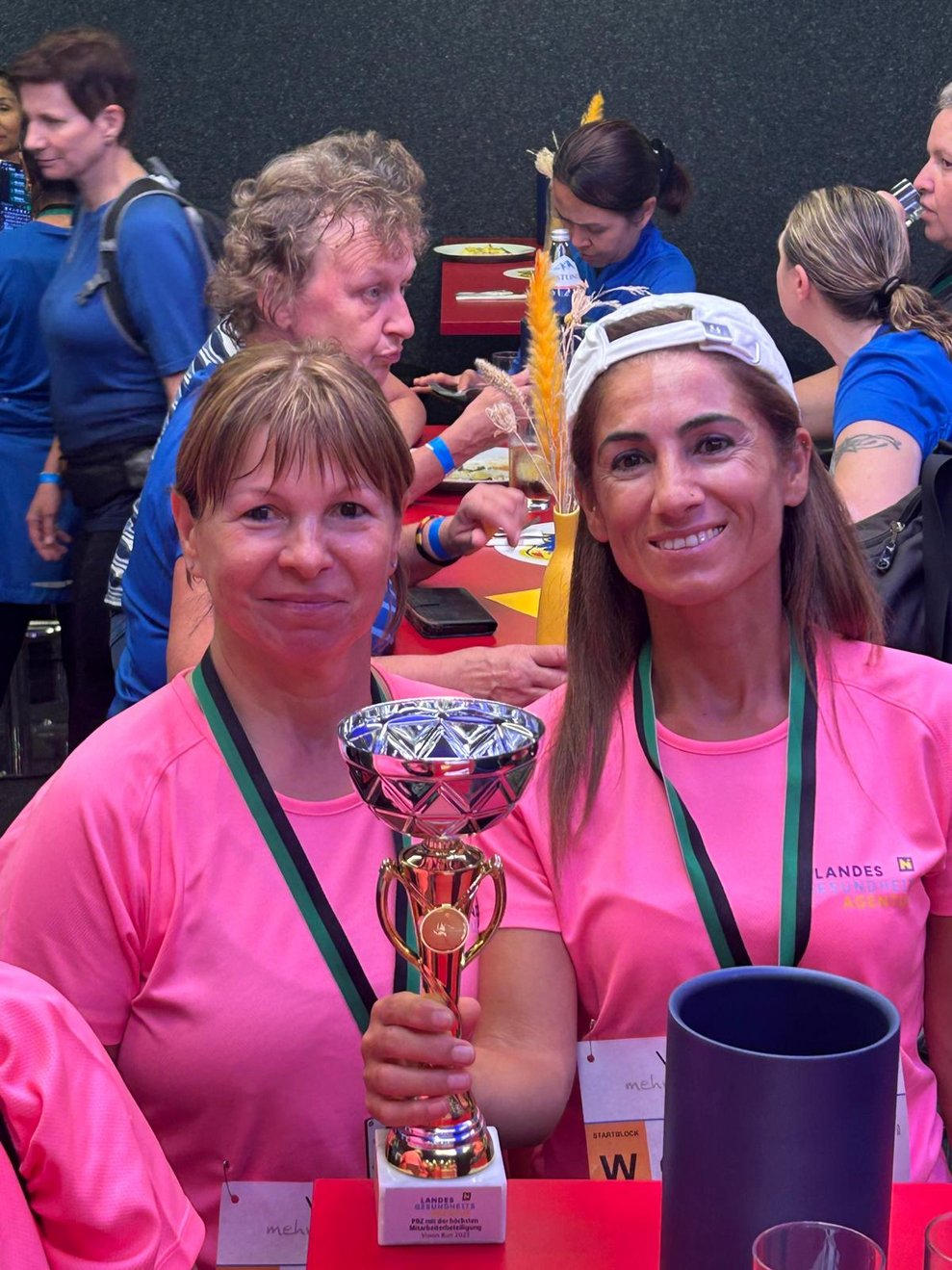 Zwei Frauen mit pinken Sport T-Shirts, Medaillen und Pokal