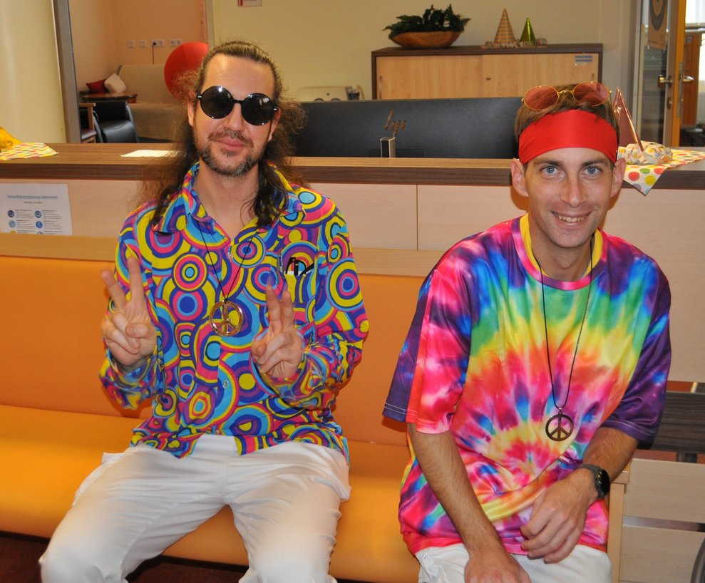 zwei Männer als Hippies verkleidet sitzen auf der Bank