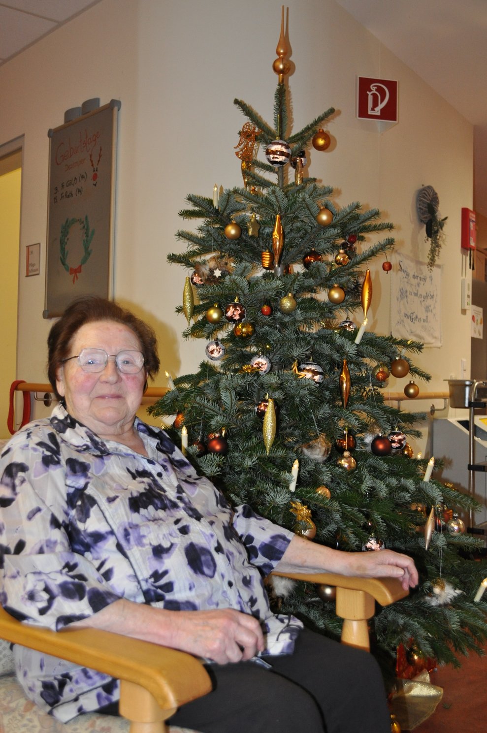eine ältere Dame sitzt vor einem geschmückten Christbaum
