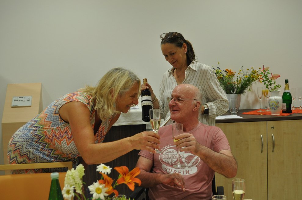 einige Menschen bei einer Geburtstagsfeier mit Blumen, Sekt und Pralinen