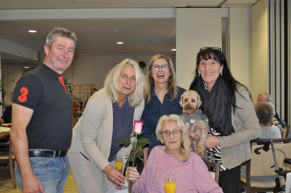 ein Gruppenfoto mit einigen Personen bei einer Geburtstagsfeiermit Pralinen, Sekt und Blumen 