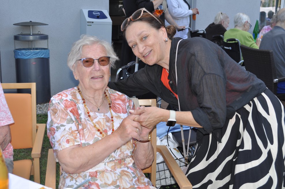 eine ältere Dame und eine Mitarbeiterin halten sich an den Händen und lachen in die Kamera