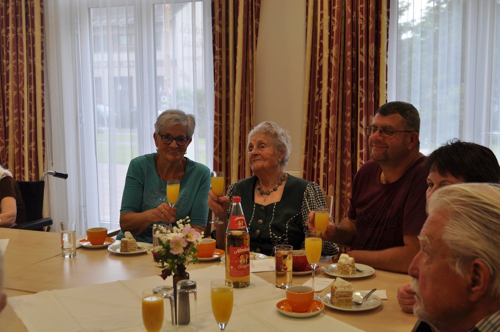 einige Menschen bei einer Geburtstagsfeier mit Blumen, Sekt und Pralinen