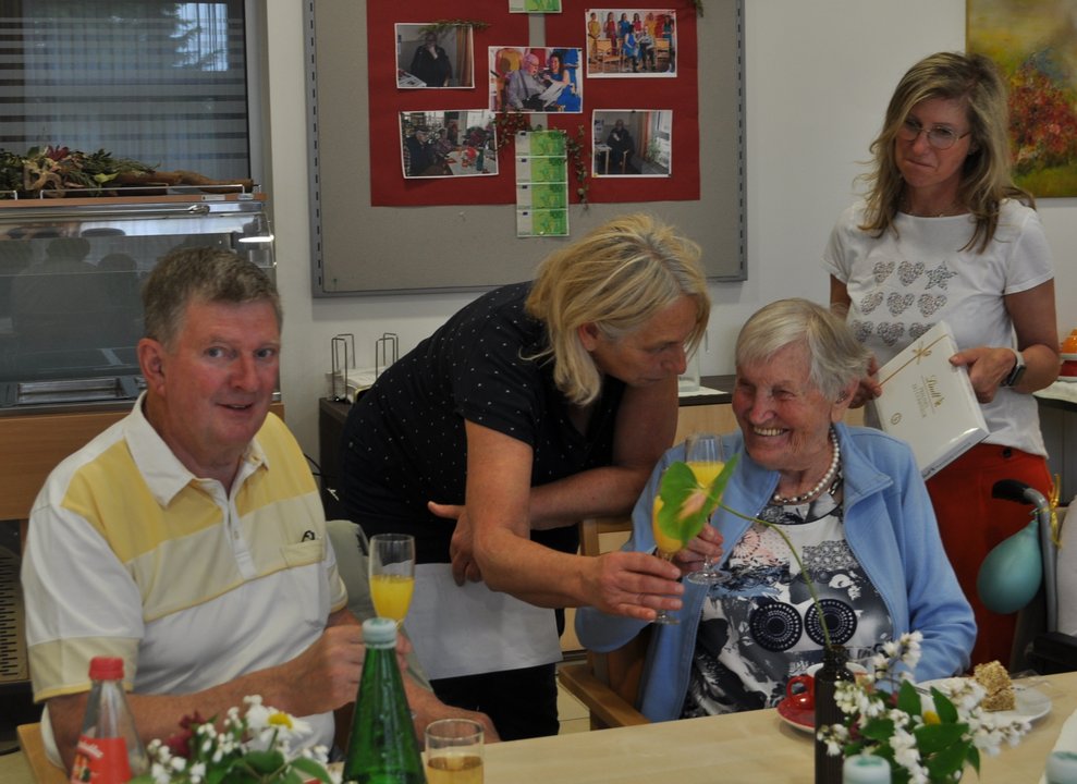 einige Menschen bei einer Geburtstagsfeier mit Blumen, Sekt und Pralinen
