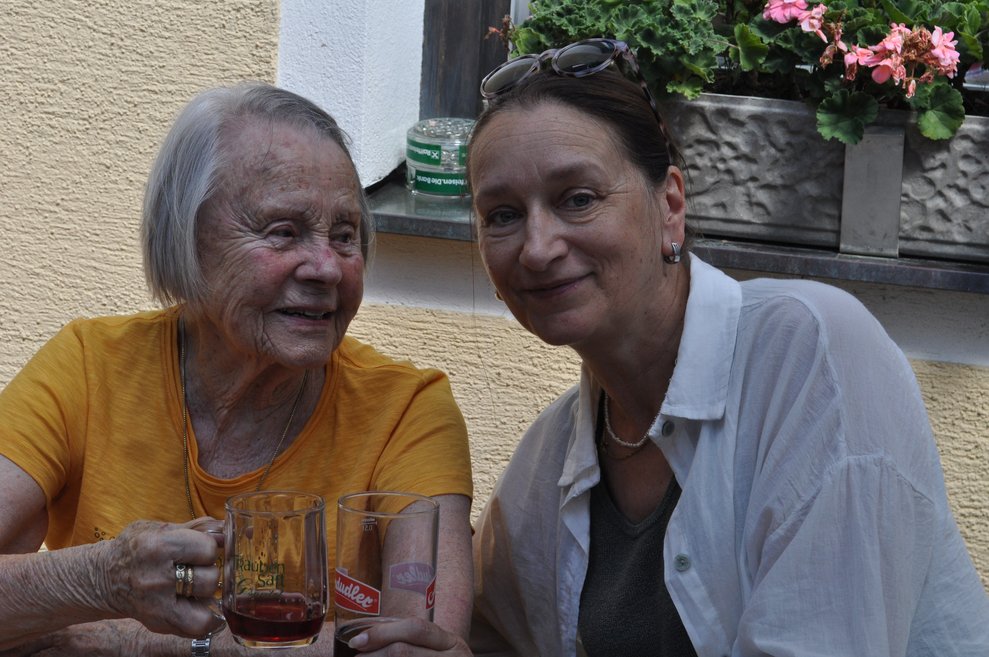 eine ältere Dame und eine jüngere Dame stoßen mit Wein an