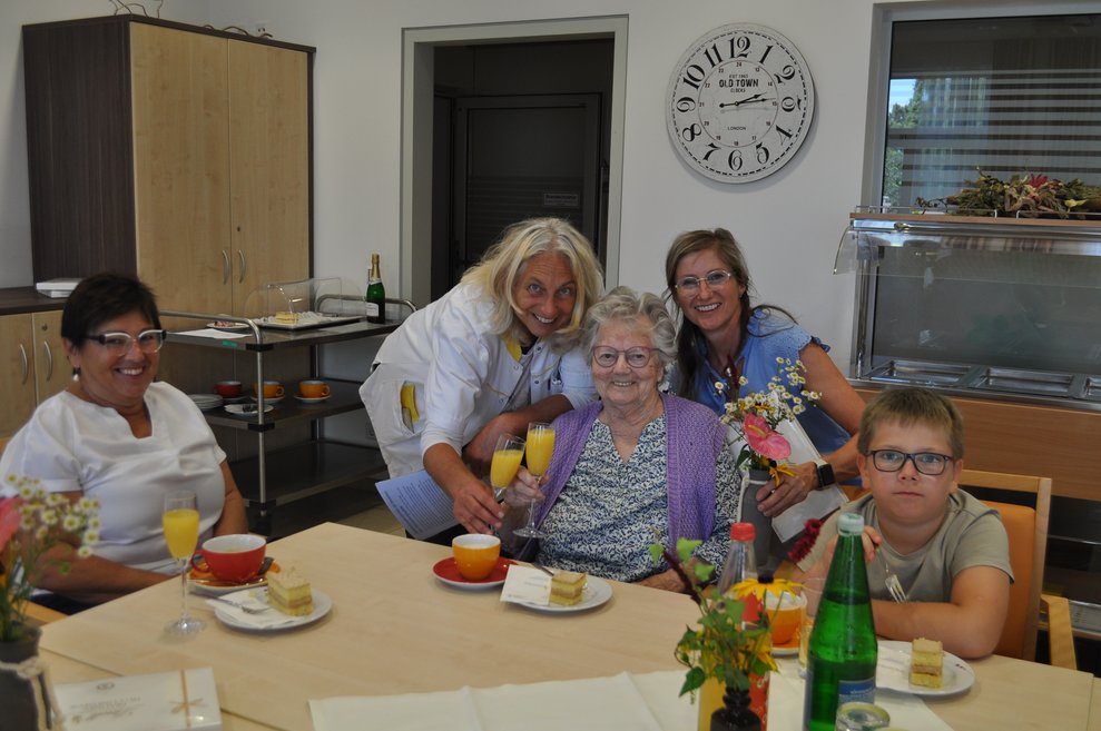eine Geburtstagsfeier mit Sekt, Kuchen und Pralinen, mehrere Personen gratulieren