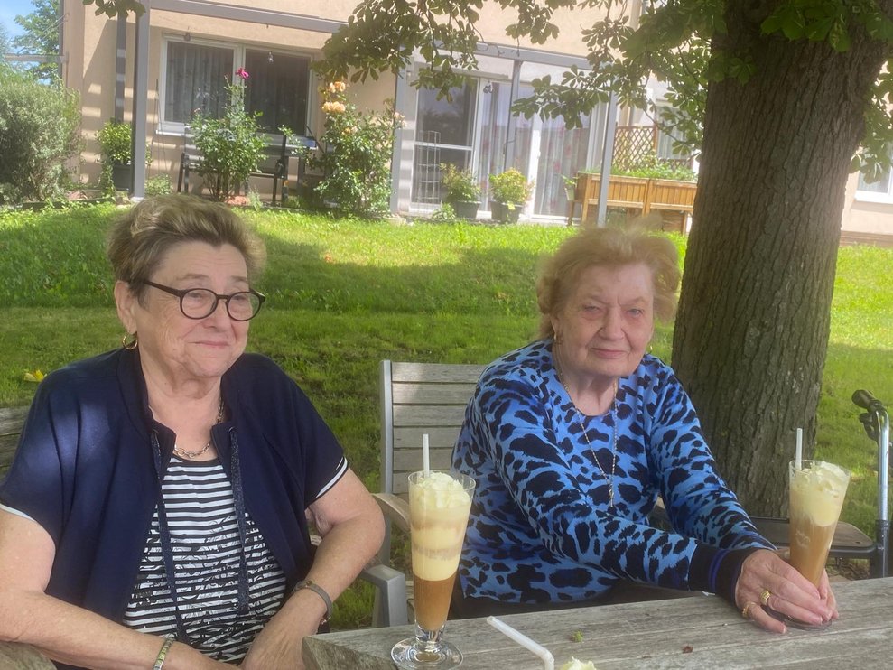 Zwei ältere Damen trinken Eiskaffee im Garten 