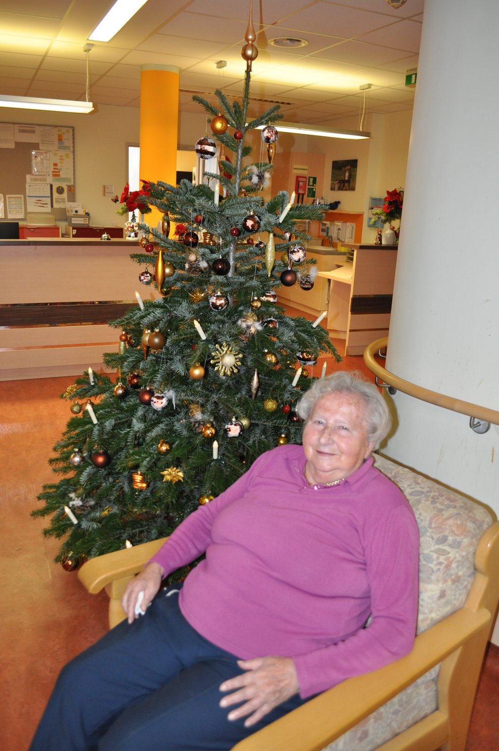 eine ältere Dame sitzt vor einem geschmückten Christbaum