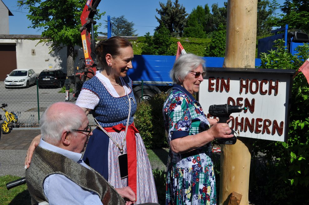 ein älterer Herr und eine ältere Dame beim Anschrauben der Tafel an den Maibaum