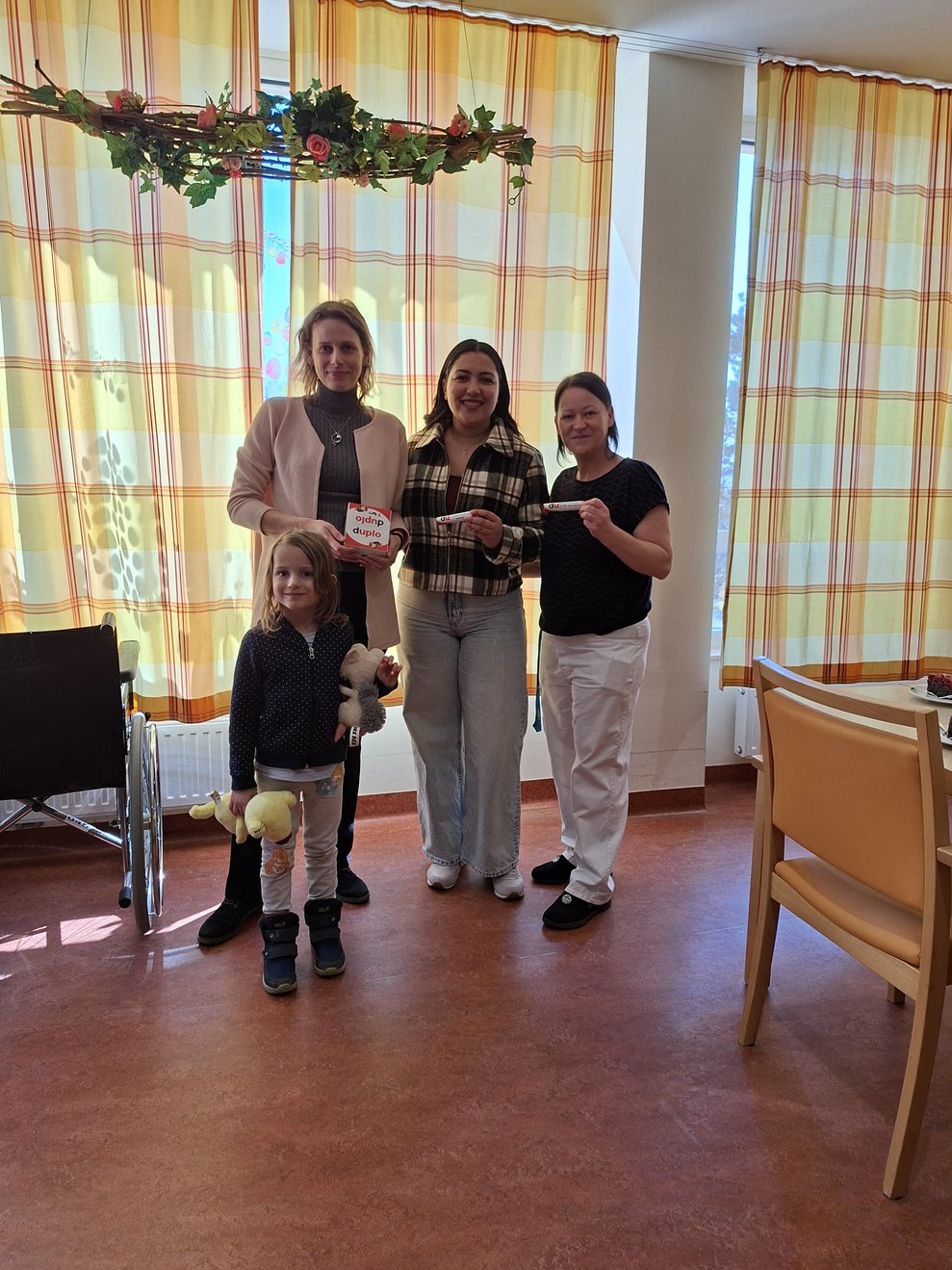 3 Mitarbeiterinnen und 1 Mädchen im Aufenthaltsbereich bei der Übergabe der Duplo Riegel.