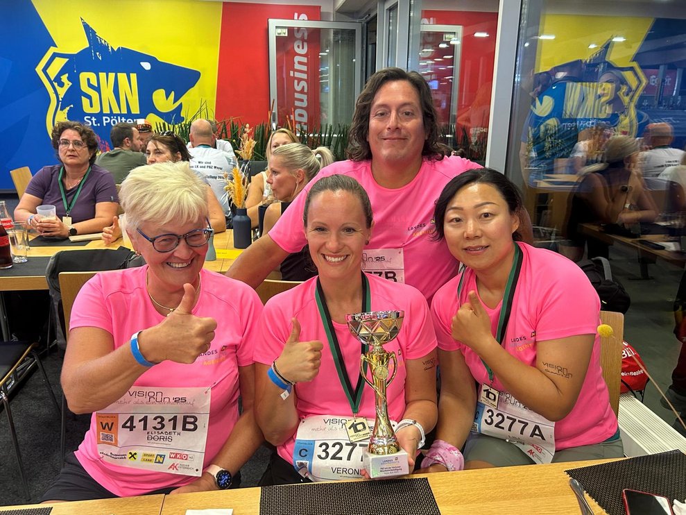 Vier Damen mit pinken Sport T-Shirts und Medaillen. Daumen hoch und eine Person hat einen Pokal in der Hand