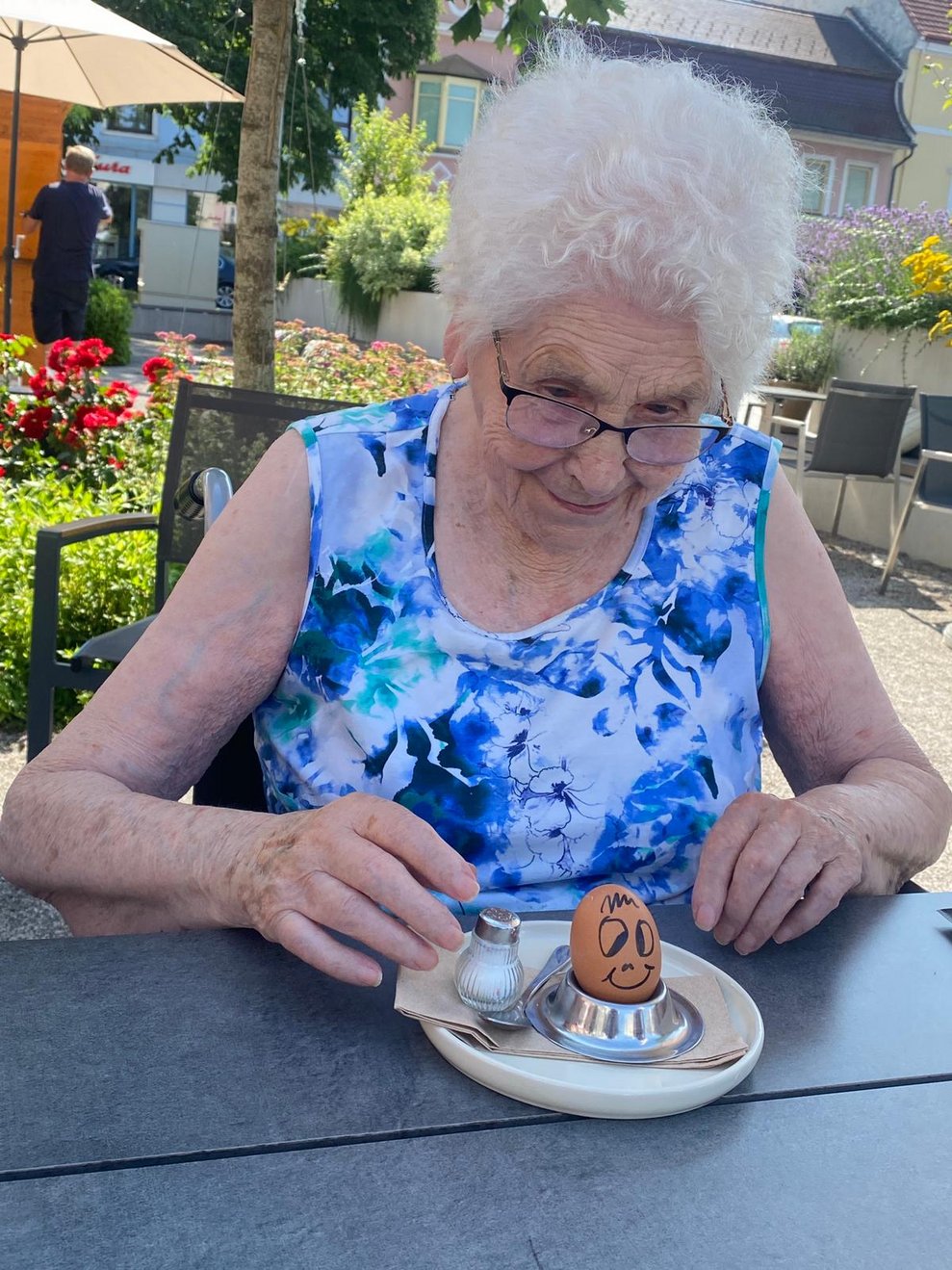 eine ältere Dame isst ein weiches Ei mit Gesicht darauf