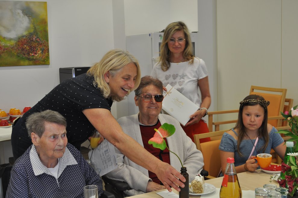 einige Menschen bei einer Geburtstagsfeier mit Blumen, Sekt und Pralinen