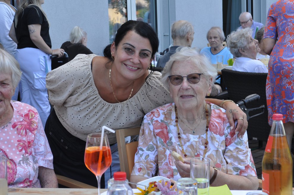 eine ältere Dame mit einer Kaffeehausmitarbeiterin mit Getränken im Garten