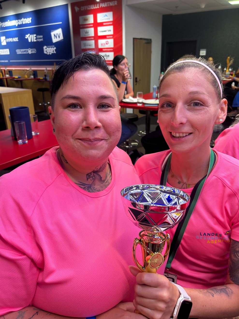 Zwei Frauen mit pinken Sport T-Shirts, Medaillen und Pokal