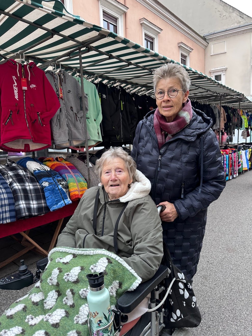 eine Dame im Rollstuhl mit einer Begleitperson am Markt